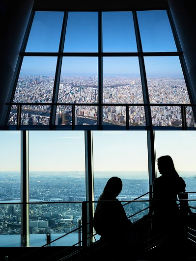 展望台の窓から一望する昼間の街並みと、窓辺で景色を楽しむ人々のシルエット