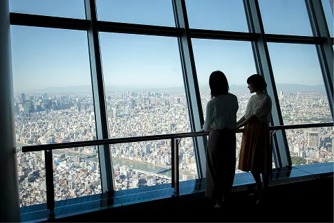 スカイツリーの展望室から東京の町並みを眺める女性2人。