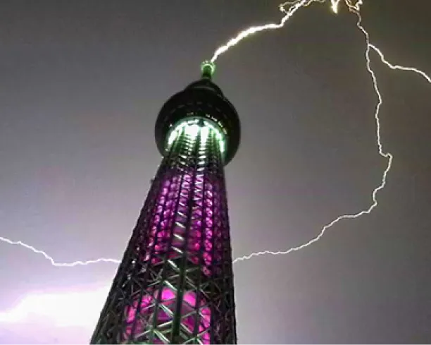 雅（みやび）のライティングが点灯した夜の東京スカイツリー頂部に、巨大な雷が直撃した劇的な瞬間の写真。