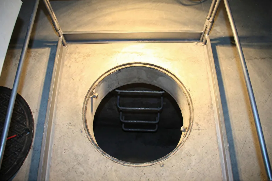 地下の広大な雨水貯留槽へと続くコンクリート製のハッチが開けられ、内部へと繋がる金属製のはしごが見える様子。