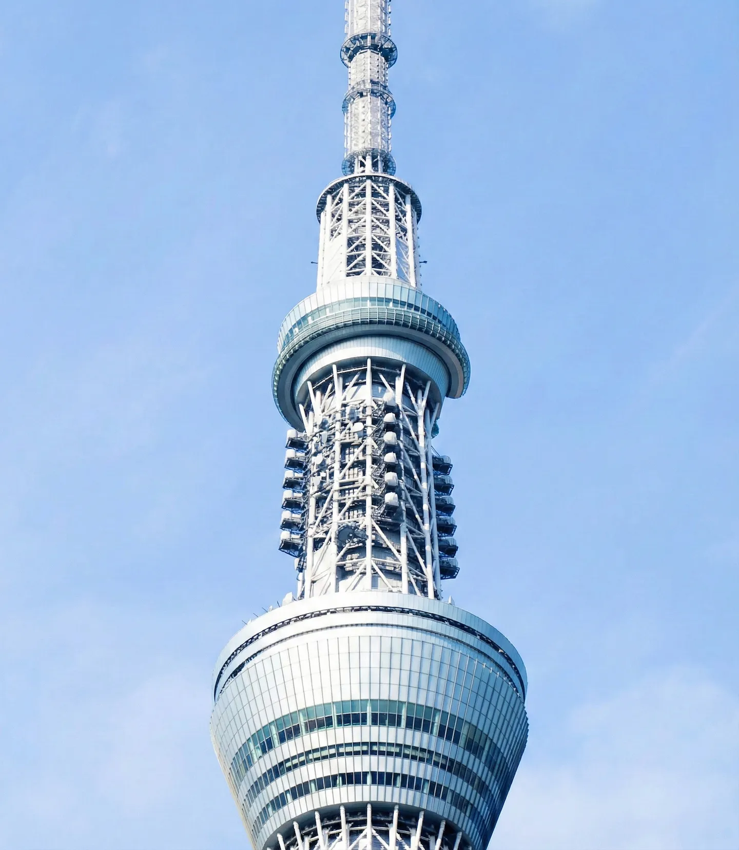 澄み渡る青空を背景に、東京スカイツリーの展望台付近を真下から見上げたクローズアップ写真。塔の複雑な鉄骨構造と近代的なデザインが強調されている。
