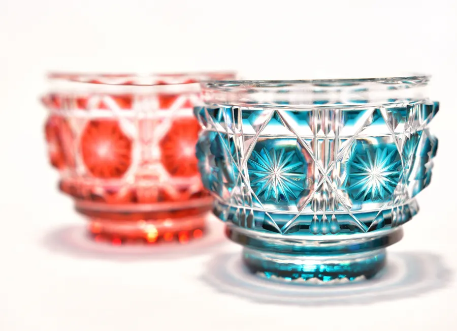 繊細なカットが施された、赤色と青色の鮮やかな江戸切子のペアグラス。伝統的な文様が光を反射して輝く、白背景のクローズアップ写真。