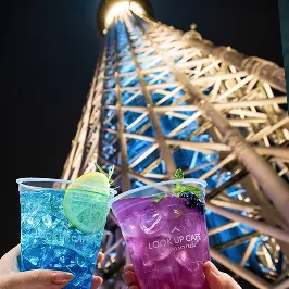 東京スカイツリーの夜景の前で紫と青のドリンクで乾杯している様子