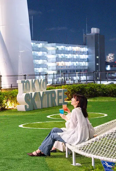 夜の芝生広場でくつろぐ女性と東京スカイツリー