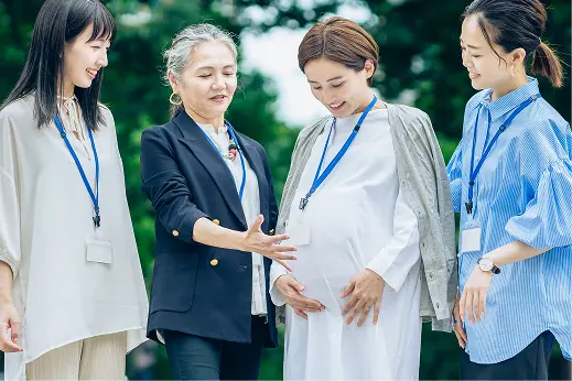 屋外で、お腹の大きい妊婦の女性社員を囲んで笑顔で話す3人の女性社員