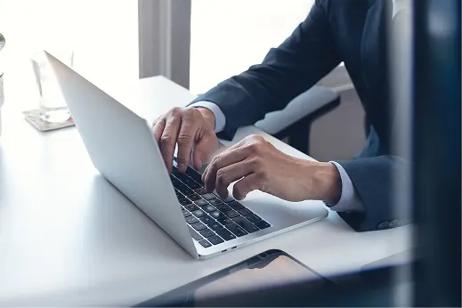 日差しの中、満開の桜の下で笑顔でこちらを見つめる、ベテランの風貌をした男性社員