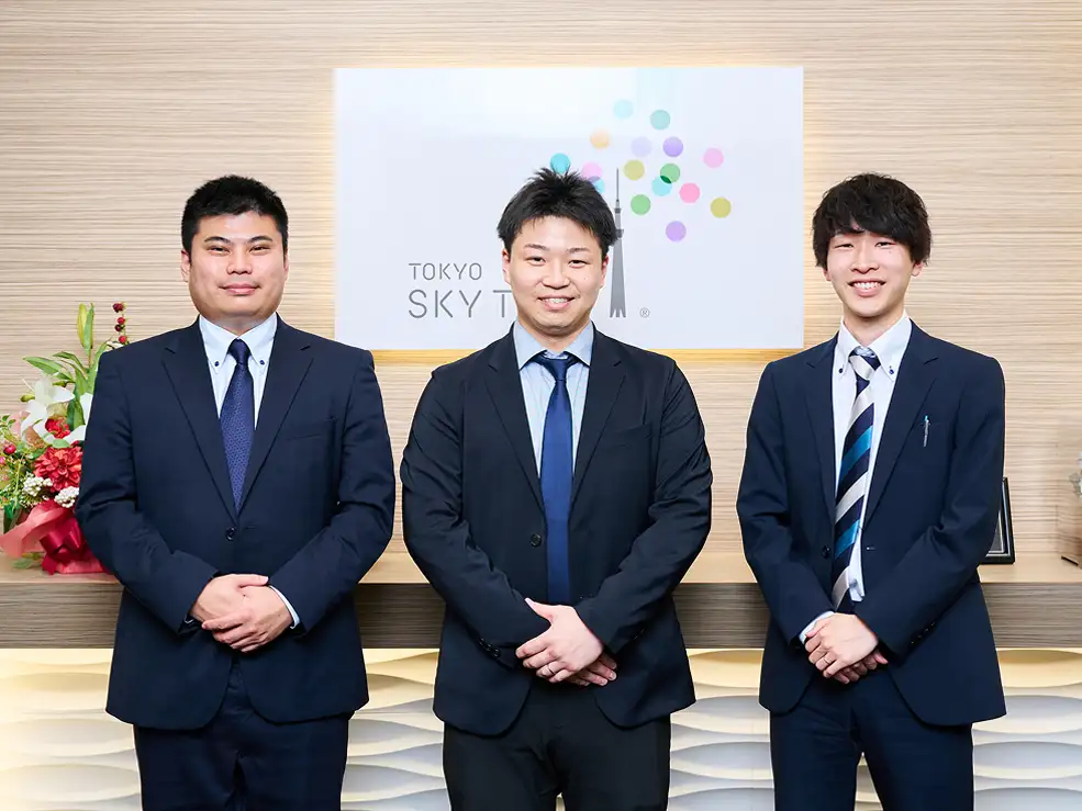 受付前で並んで立つスーツ姿の男性スタッフ3名