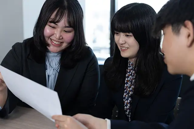 オフィスのような場所で、3人の男女が書類を一緒に見ながら和やかに打ち合わせをしている様子。