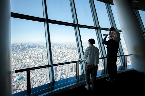 展望台のガラス越しに、眼下に広がる街並みを眺める親子（大人1名、子供1名）