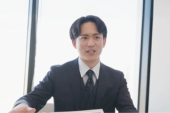 屋内（窓際）でスーツを着用し、資料を見ながら話をする男性社員