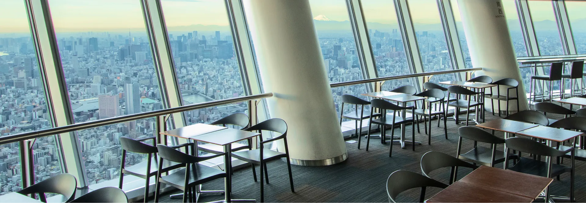 テーブルに並ぶ、東京スカイツリーをモチーフにした彩り豊かなメニュー。星形のライスが添えられたカレーや、スカイツリーのラテアートが施されたカフェラテ、公式キャラクター「ソラカラちゃん」のピックが飾られた爽やかなブルーのパフェなどが、食事を楽しむ人々の手元とともに写っています。