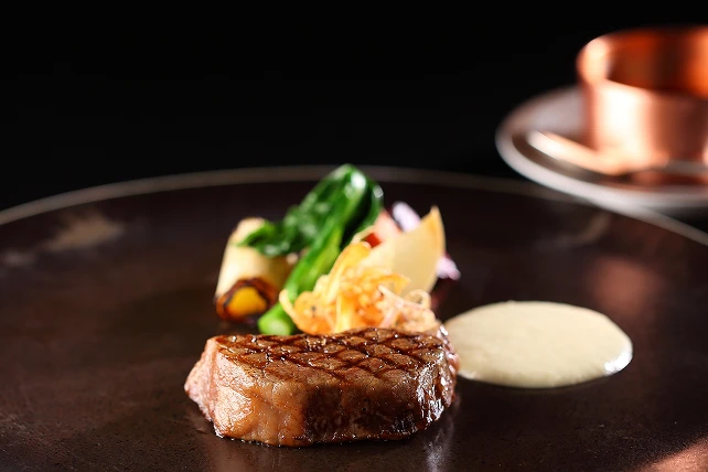 夜の帳が下りた東京の煌めく夜景を眼下に望む、落ち着いた雰囲気の店内。弧を描く大きな窓に沿ってテーブル席がゆったりと配置されています。