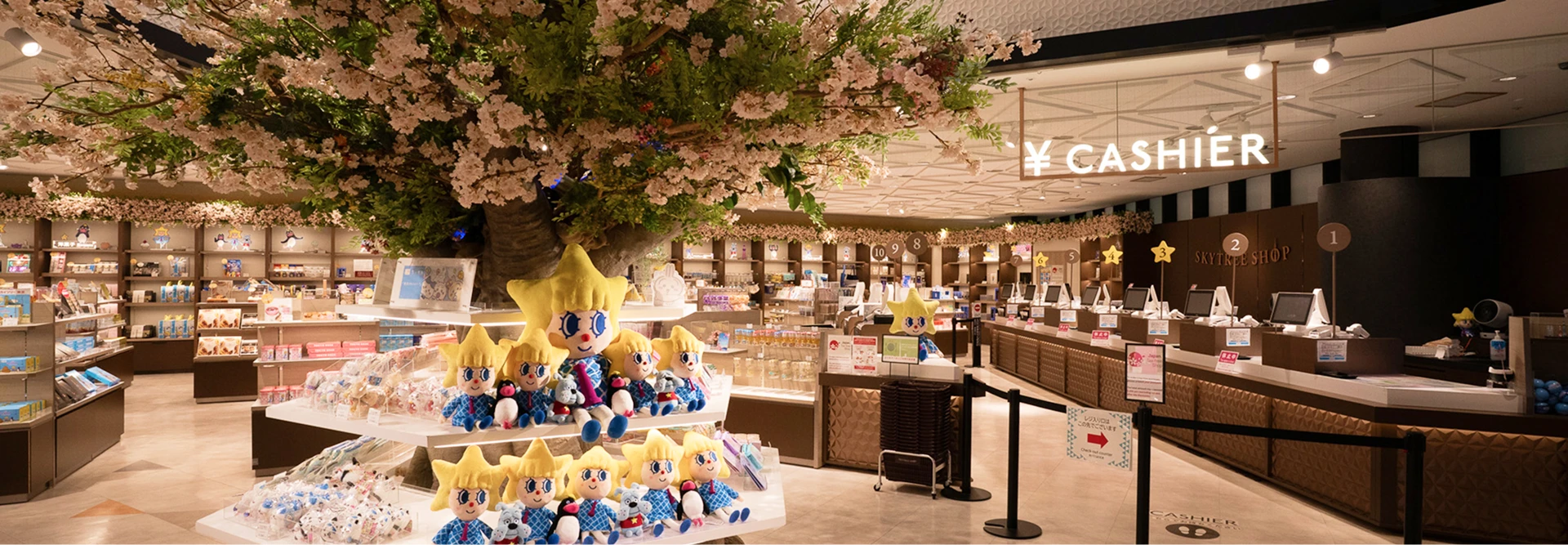 東京スカイツリーの公式キャラクター「ソラカラちゃん」のぬいぐるみが並ぶ円形の棚や、中央に配置された大きな桜の装飾木が目を引く、明るく広々とした店内の様子。