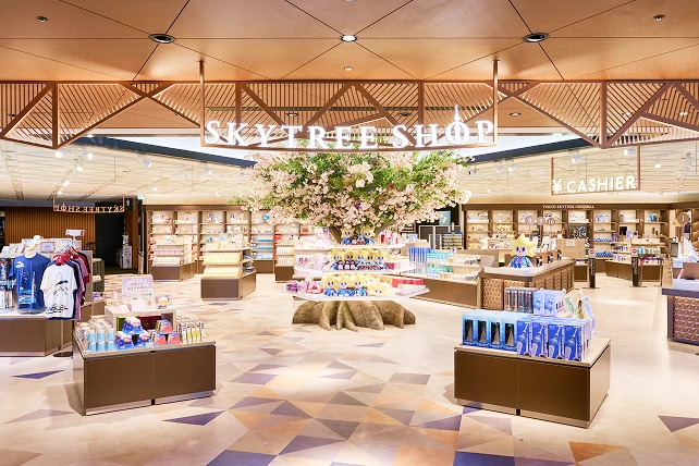 「SKYTREE SHOP」のロゴが掲げられた、明るくモダンな店内の様子。中央には満開の桜を模した大きな装飾木があり、その下の円形の棚には公式キャラクター「ソラカラちゃん」のぬいぐるみが並んでいます。